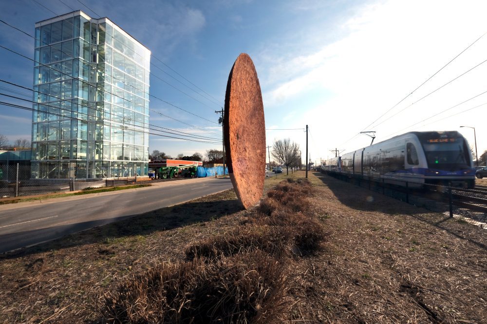 A futuristic, 71-foot lighted glass car vending machine from the online auto dealer Carvana sits at the Scaleybark Station along Charlotte's Blue Line light rail. From 1955 to 2007 the site was home to the iconic South 21 Drive-In, where carhops serving motorists evoked the '50s and '60s. At center is Thomas Sayre's sculpture, "Furrow," modeled on farmers' disc harrows and commemorating the agricultural past that predated Charlotte's 19th- and 20th-century industrial growth. 