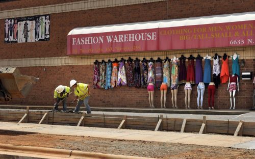 Crews work on a parking lane, curb, gutter and sidewalk in front of Fashion Warehouse, North Tryon Street at Tom Hunter Road. Owner George Saini, who hangs clothes outside “New York style,” says he is happy the construction will provide more parking and a more walkable approach to his store. Photo: Nancy Pierce